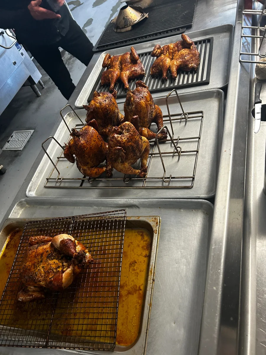 Roasted whole chickens resting on racks and trays in a professional kitchen