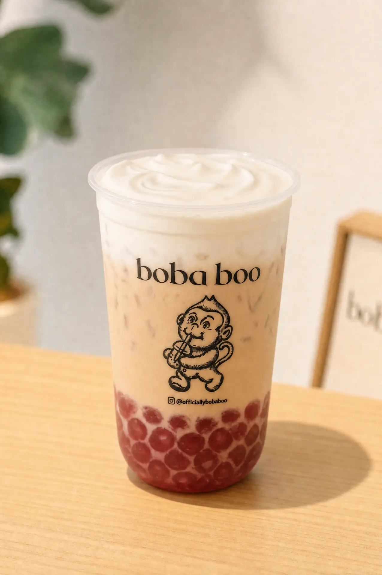 boba boo milk tea with cream top and red boba pearls in a branded cup