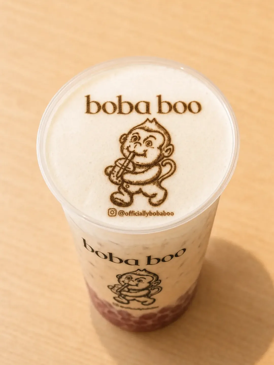 Boba milk tea cup with the boba boo monkey logo and @officiallybobaboo handle printed in cocoa on the foam, on a wood table
