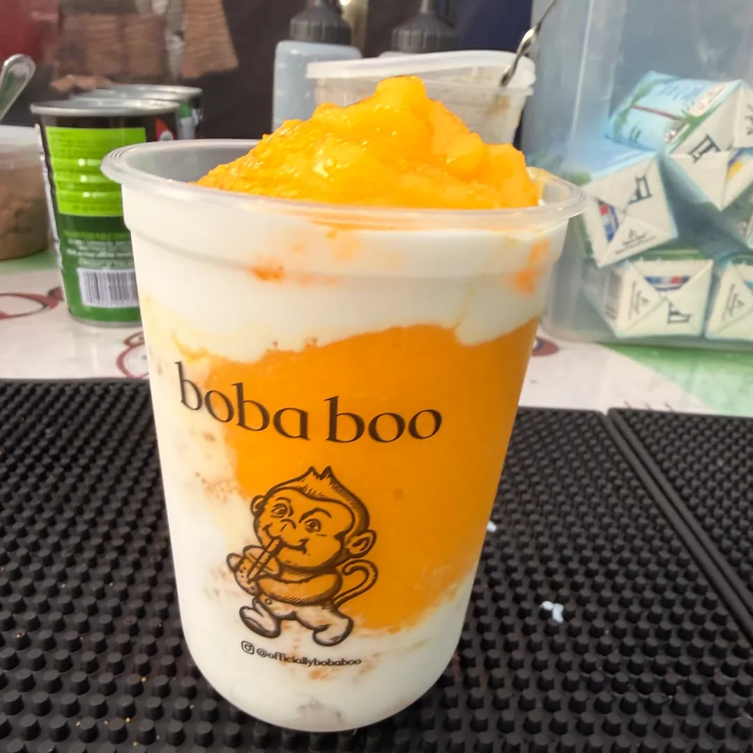 Mango and cream drink topped with fresh mango chunks on a black bar mat