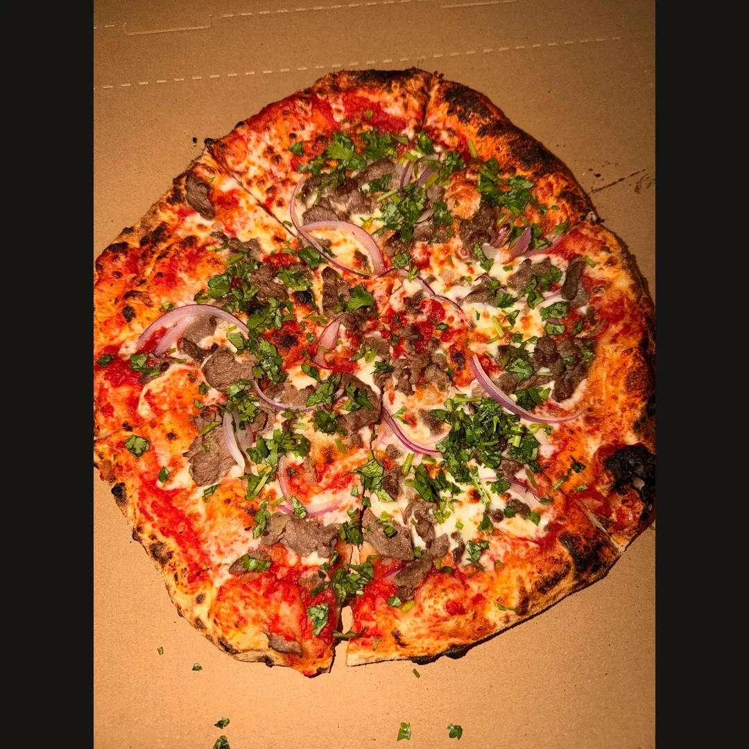 Fresh herb-topped pizza with red onion and melted cheese in a box