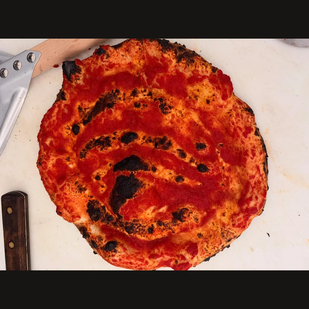 Tomato-sauce pizza base with a charred, blistered crust on a preparation board