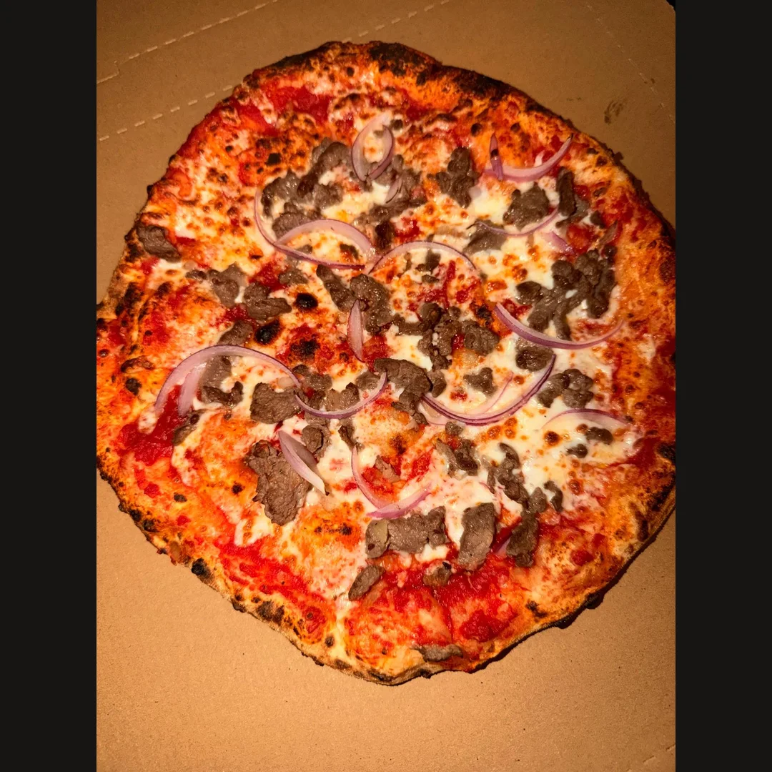 Neapolitan pizza topped with meat, melted cheese and red onion in an open box