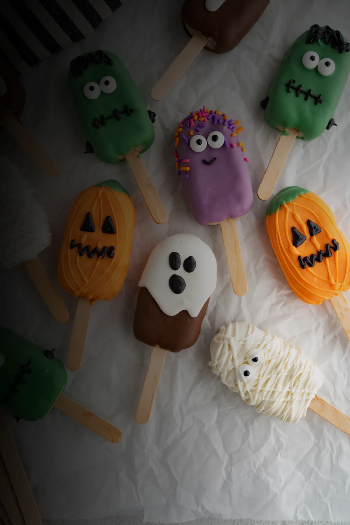 Custom Cake Pops: Halloween cake pops — pumpkins, Frankenstein monsters, a ghost, a mummy and a sprinkle monster — arranged on parchment paper