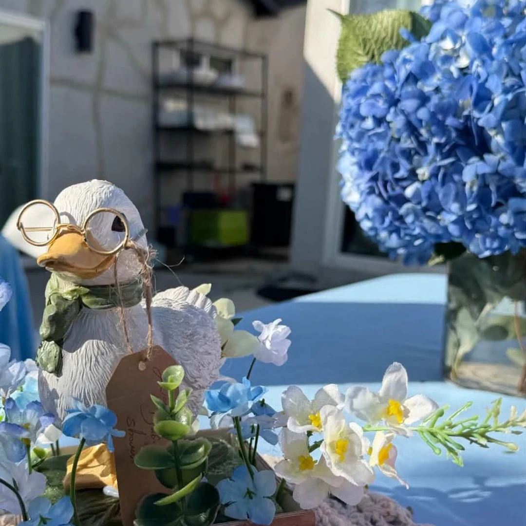 Storybook duck centerpiece with glasses, blue hydrangeas and white flowers on a lace-covered table