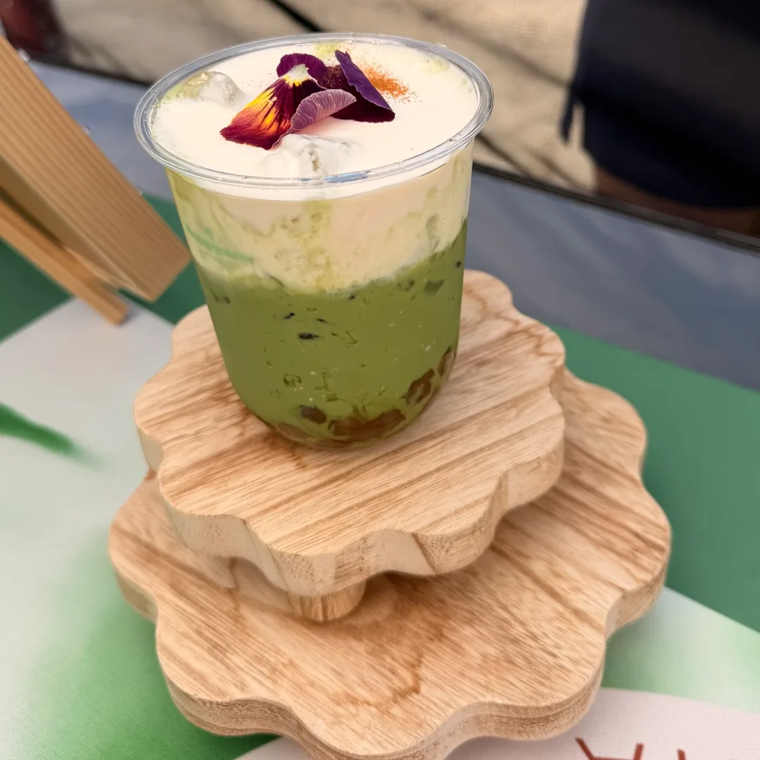 Matcha latte with cold foam and an edible pansy flower on stacked wooden risers