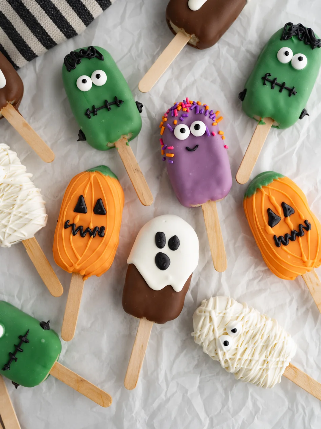 Assorted Halloween cake pops including pumpkins, Frankenstein monsters, a ghost and mummies on parchment paper