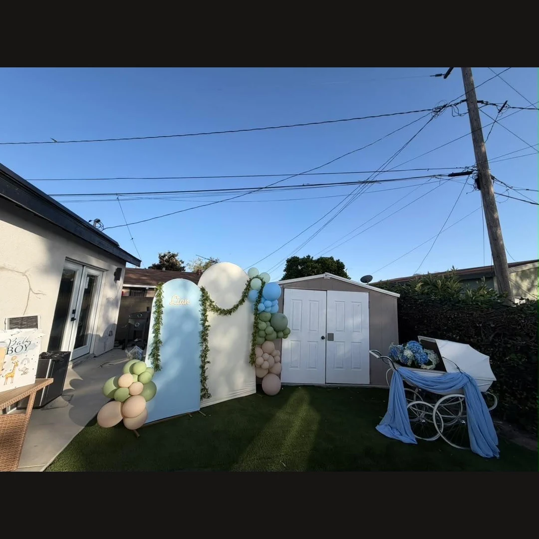 Backyard celebration with blue and cream balloon arches, greenery and a blue-draped white carriage