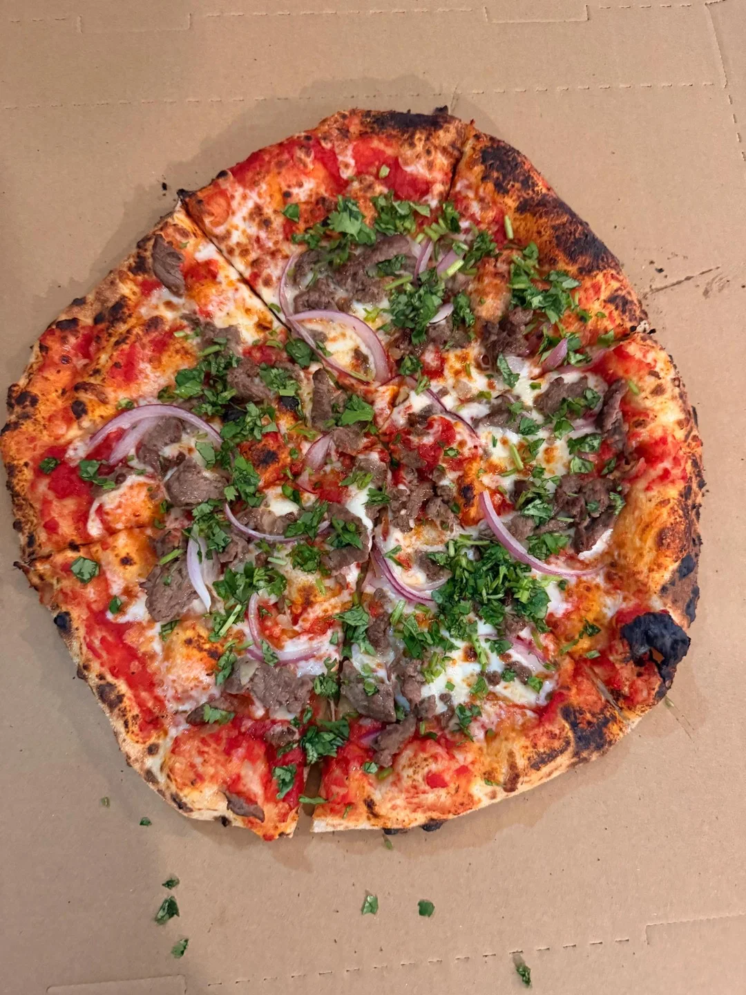 Neapolitan pizza topped with meat, red onion and fresh herbs in an open box