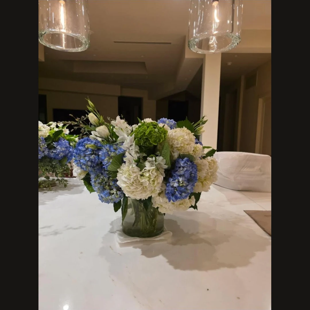 Blue and white hydrangeas with greenery in a glass vase on a marble counter