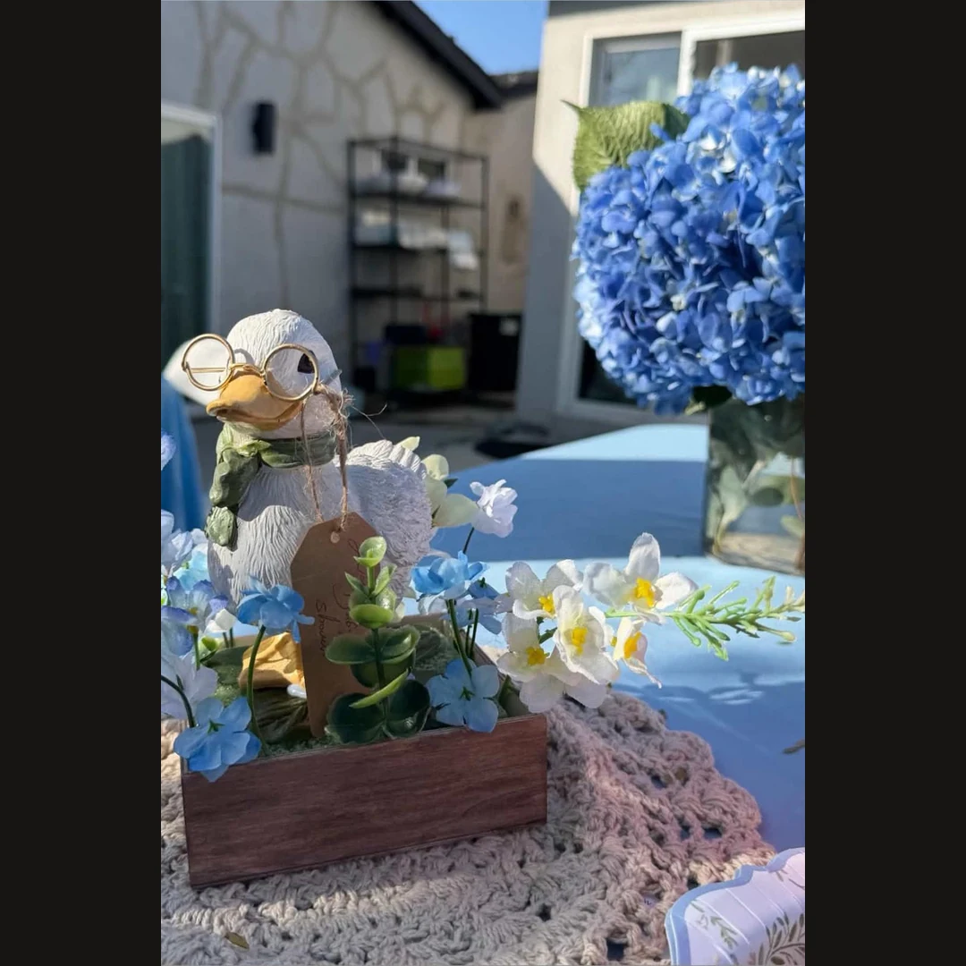 Storybook duck centerpiece surrounded by blue hydrangeas and white flowers