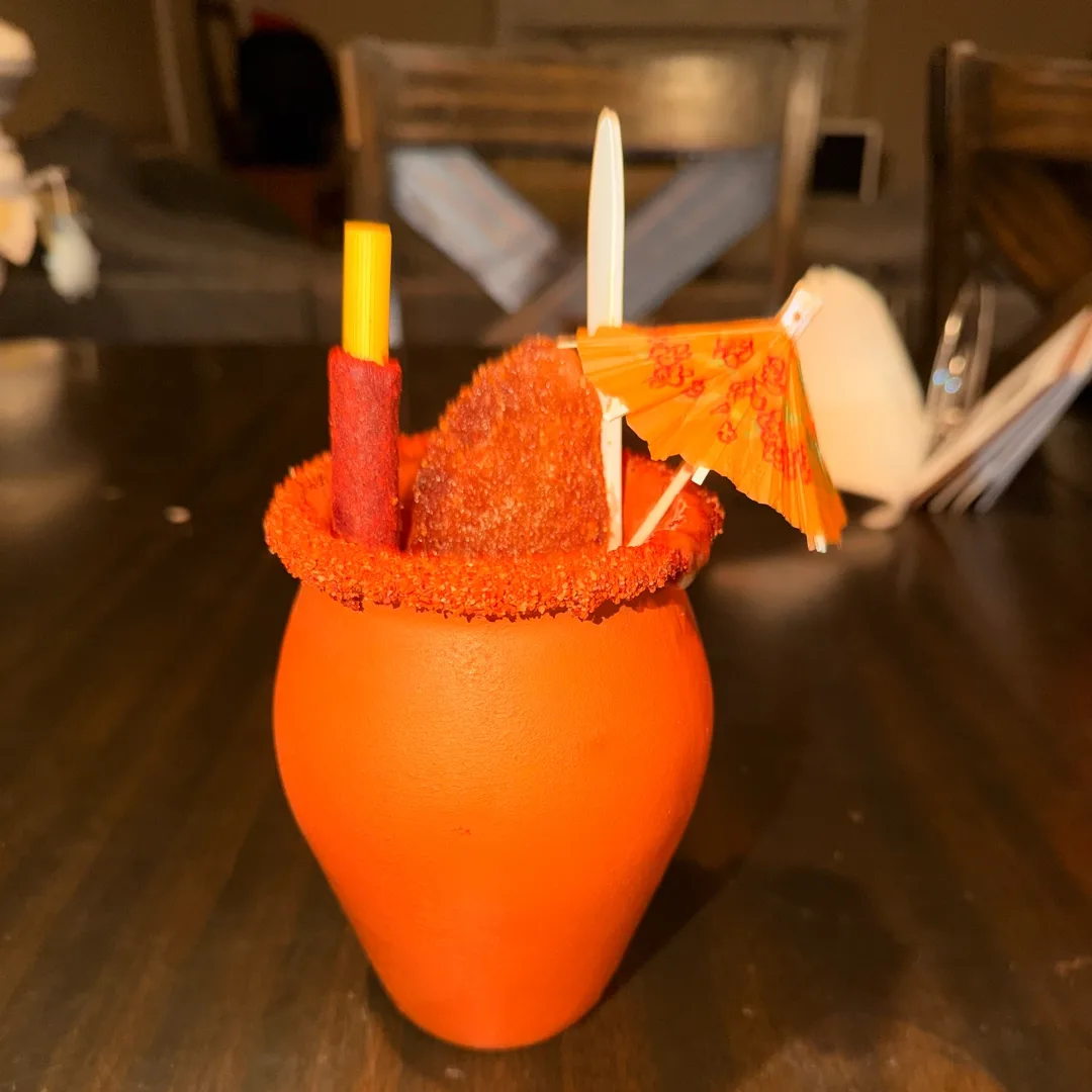 Clay cup mocktail with a chili rim, tamarind straw and an orange paper umbrella