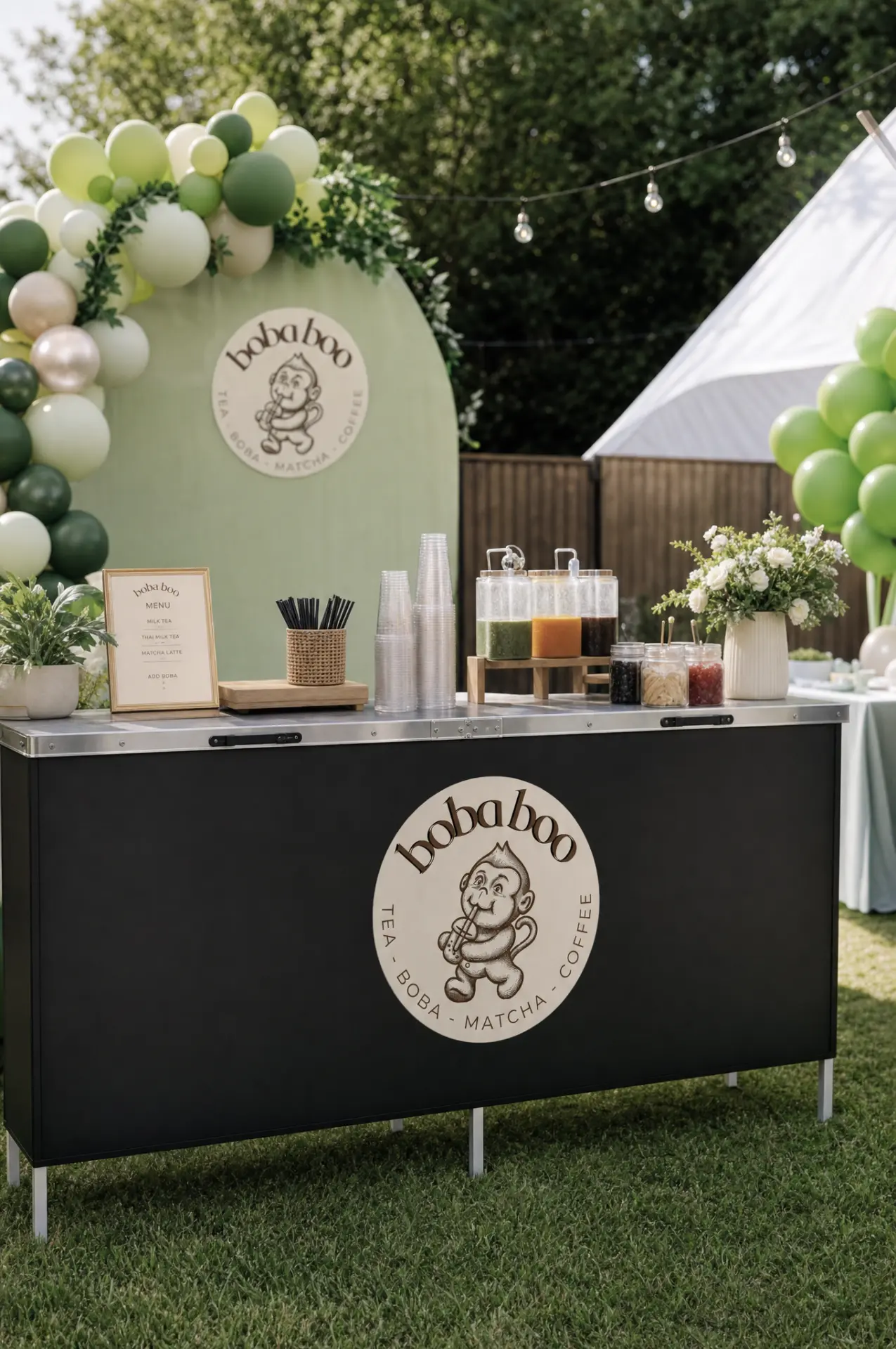 boba boo backyard event bar with fruit tea dispensers, topping jars and a green balloon arch