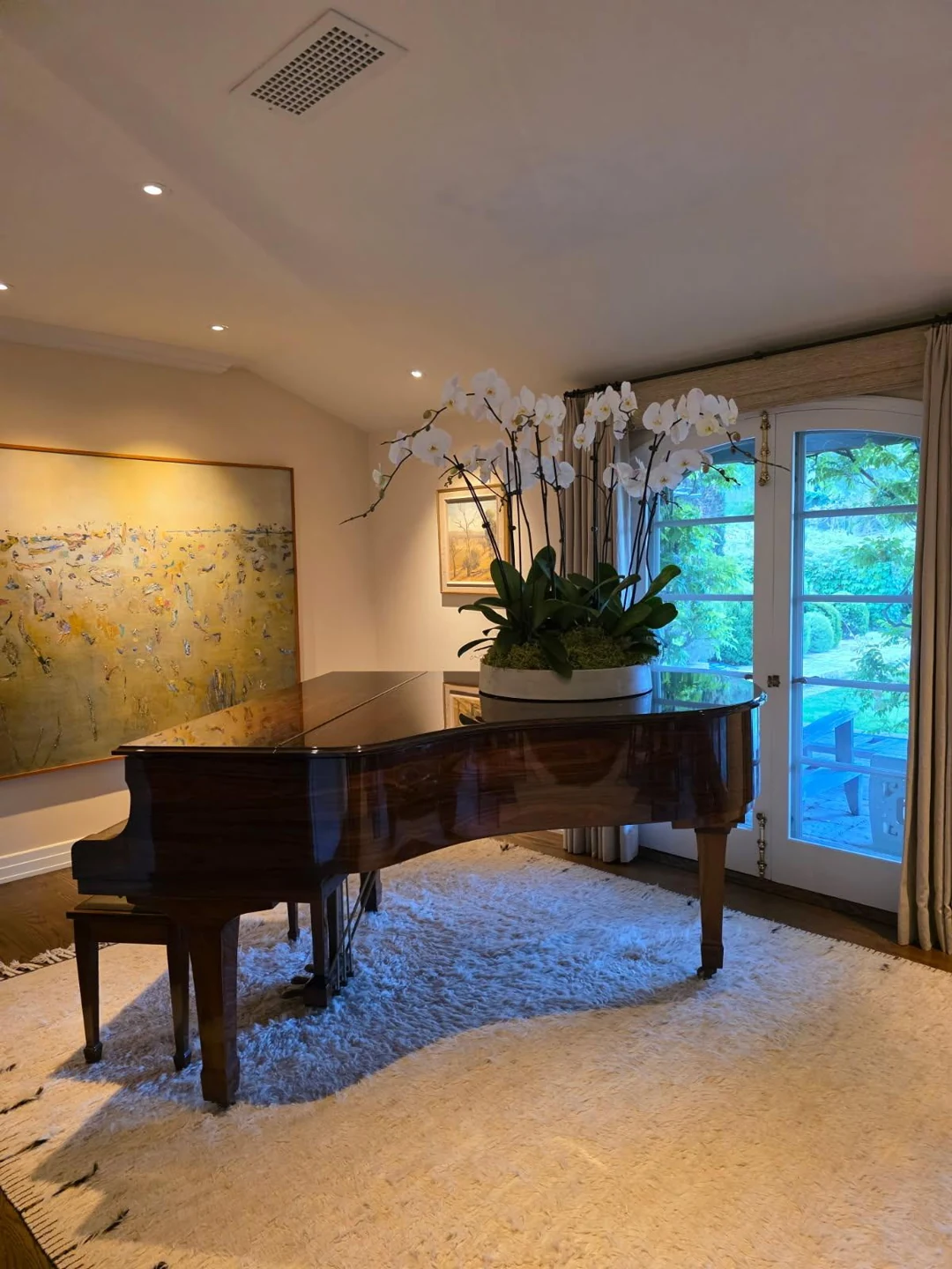 White orchid arrangement with glossy green leaves displayed on a grand piano