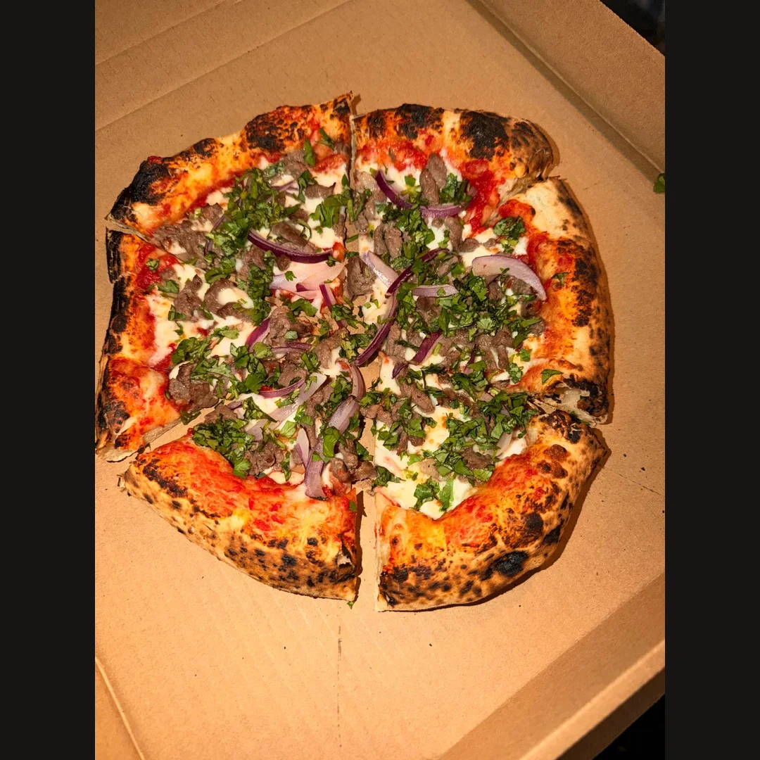 Sliced pizza topped with meat, red onion and fresh herbs in a box