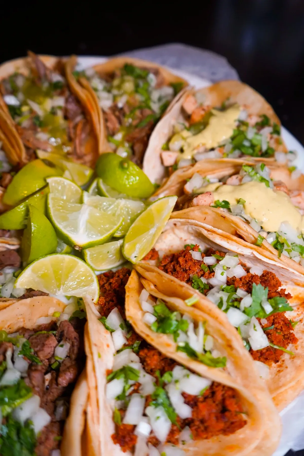 A ring of soft-tortilla tacos topped with onion and cilantro around a cluster of lime wedges