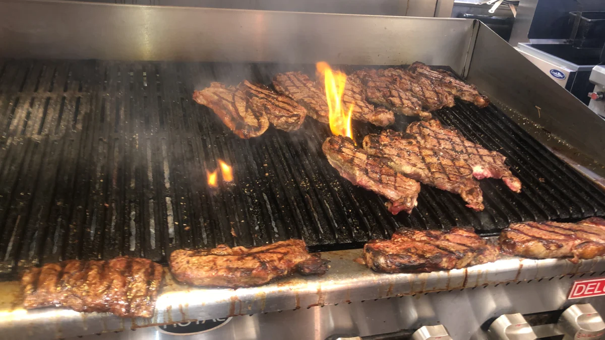 Steaks cooking over flames on a commercial grill